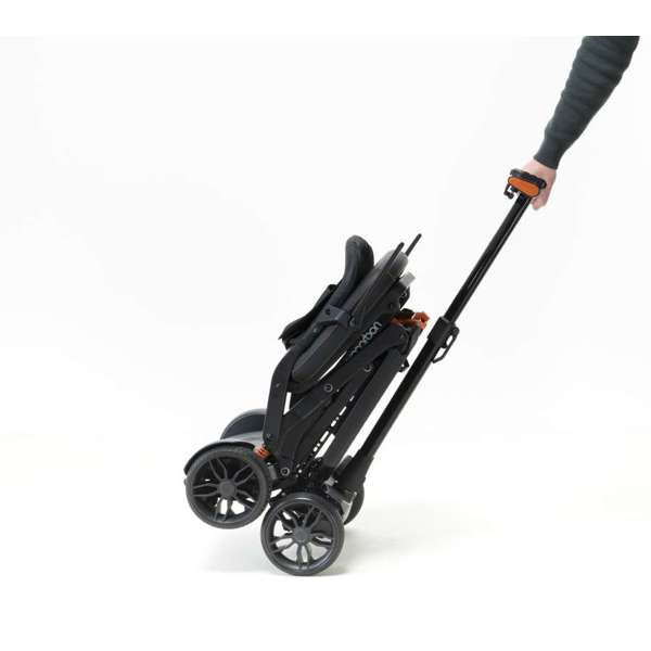 A person pulls a folded black pushchair by its handle on two wheels against a white background.